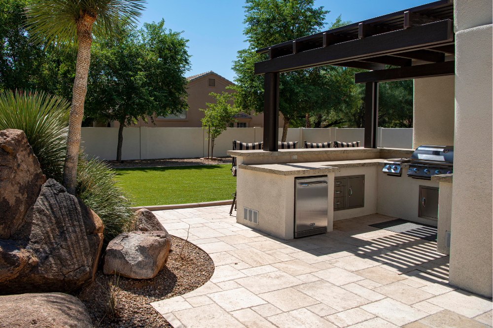 Outdoor kitchen installation with a concrete countertop, built-in grill, refrigerator, and shaded pergola.