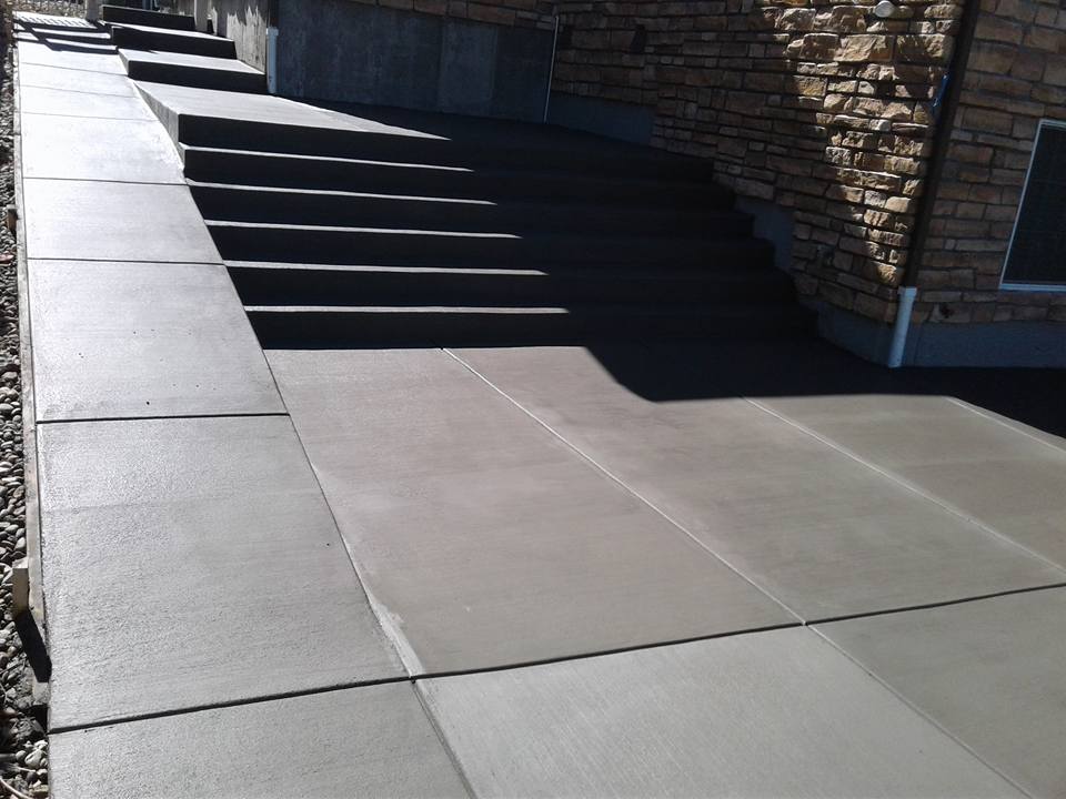 Concrete steps lead to a house, flanked by a stone wall, showcasing a well-designed landscape by a professional company.