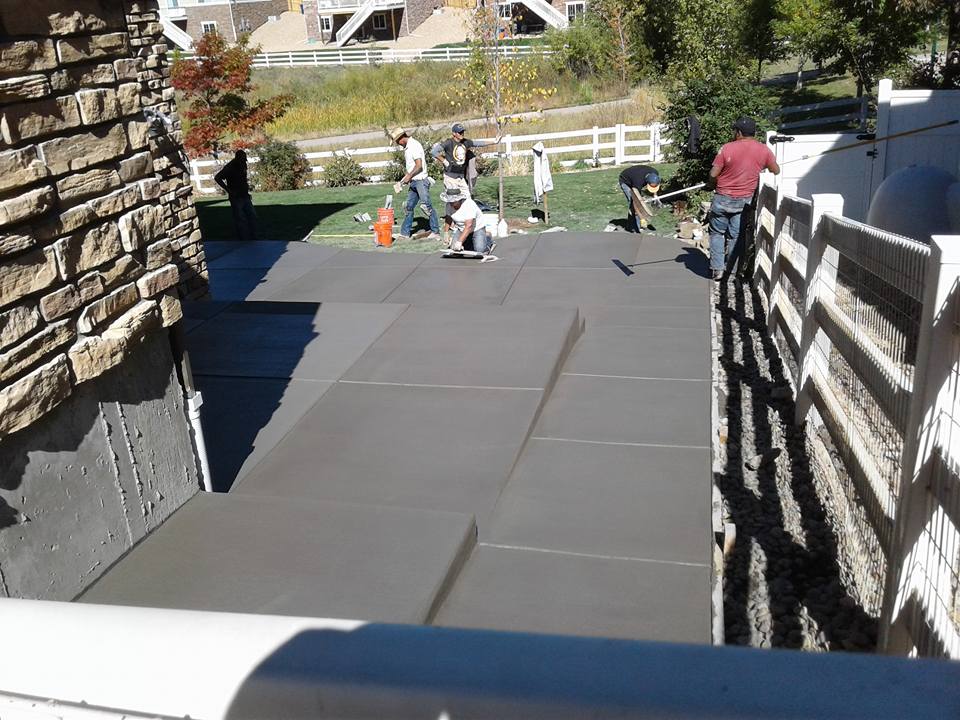 Concrete patio being installed by a landscape company, showcasing tools and materials in a residential outdoor setting.