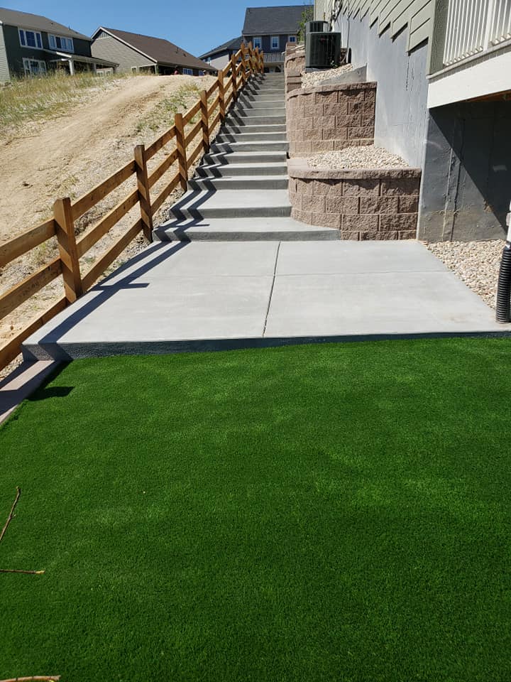 Artificial grass in front of a house with steps, showcasing a well-maintained landscape by a professional landscape company.