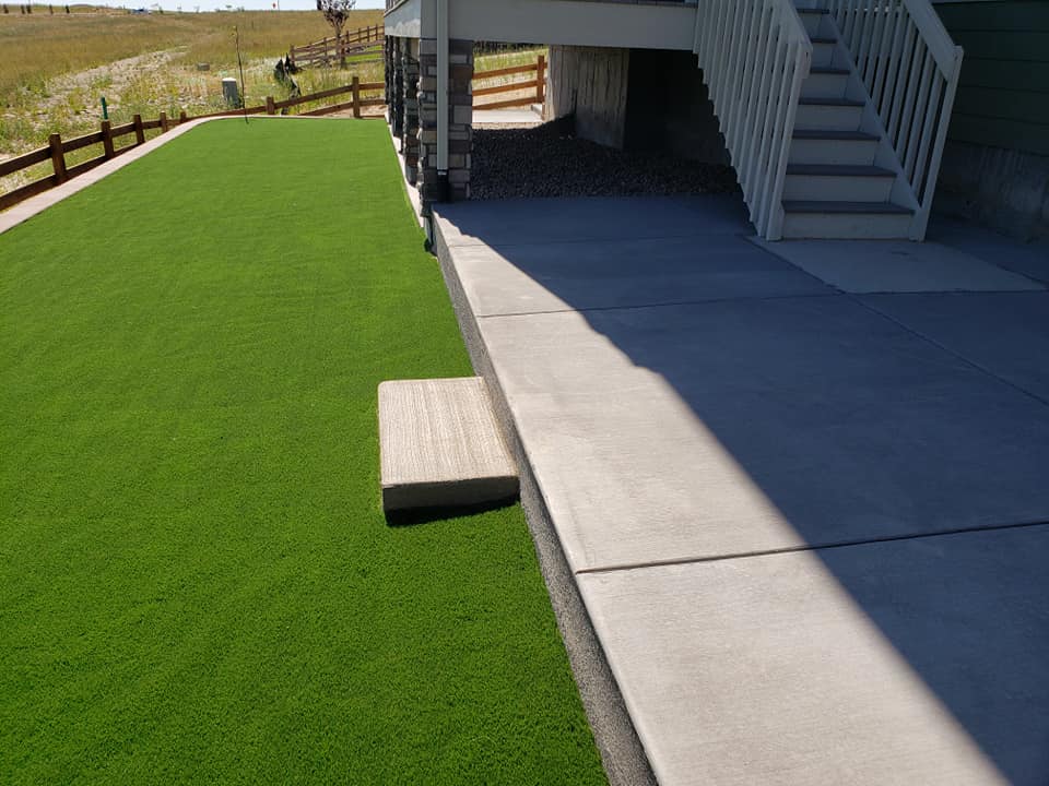 Artificial turf installed in front of a house, featuring stairs, showcasing the work of a landscape company.