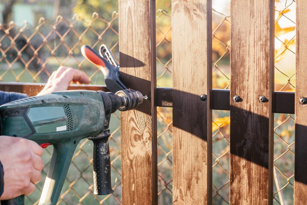 Person using a power drill to fasten screws during fence repair on wooden boards.