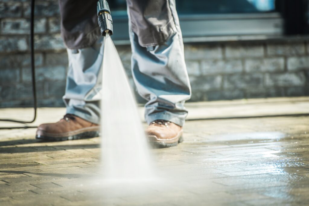 Man pressure washing residential concrete driveway to remove dirt and stains.